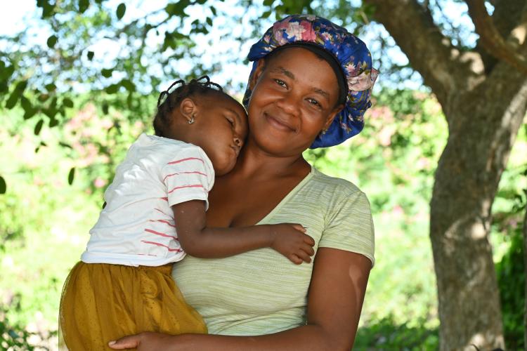 A Haitian woman holds her sleeping toddler daughter in her arms.